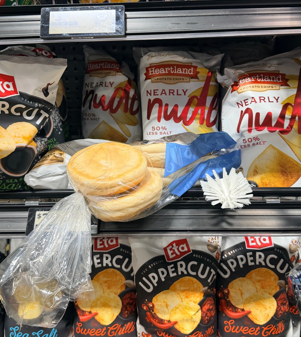 chips on display in a supermarket shelf. Stuck amongst the chips are a hamburger bun pack and cleaning brush