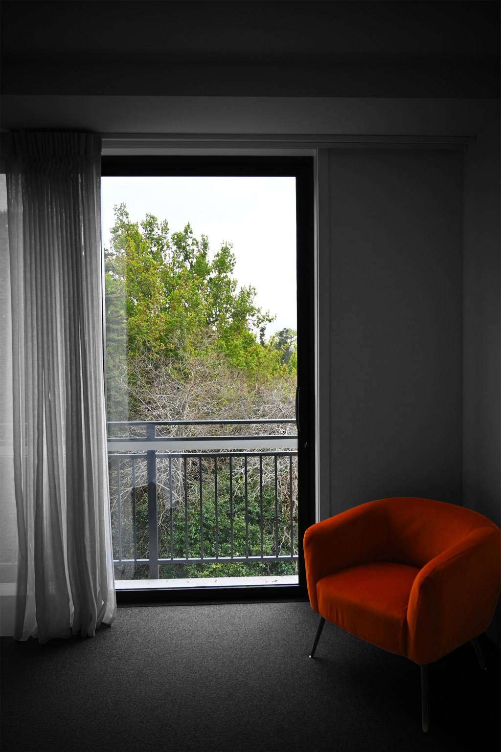 Open window with view of trees, plush orange chair to the side